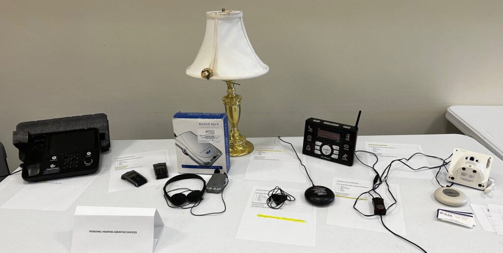 A table displaying a variety of assistive listening devices including amplification, fire alarm, doorbell notification, etc.