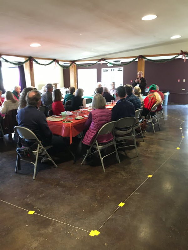 People eating at potluck, sitting at 2 long tables with temporary hearing loop around the perimeter on the floor